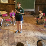 Photo of educator surrounded by kids in barn