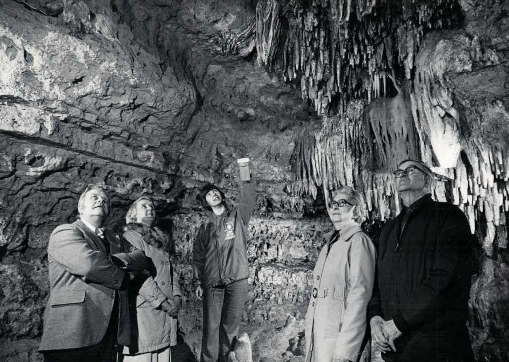 Black and white photo of people looking up at cave formations