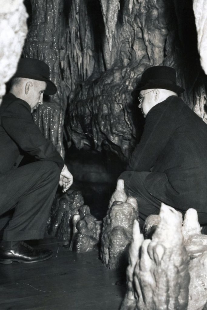 Two men crouch in the cave discussing options to build a manmade tunnel.
