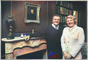 Man and woman pose in front of fireplace and portrait.