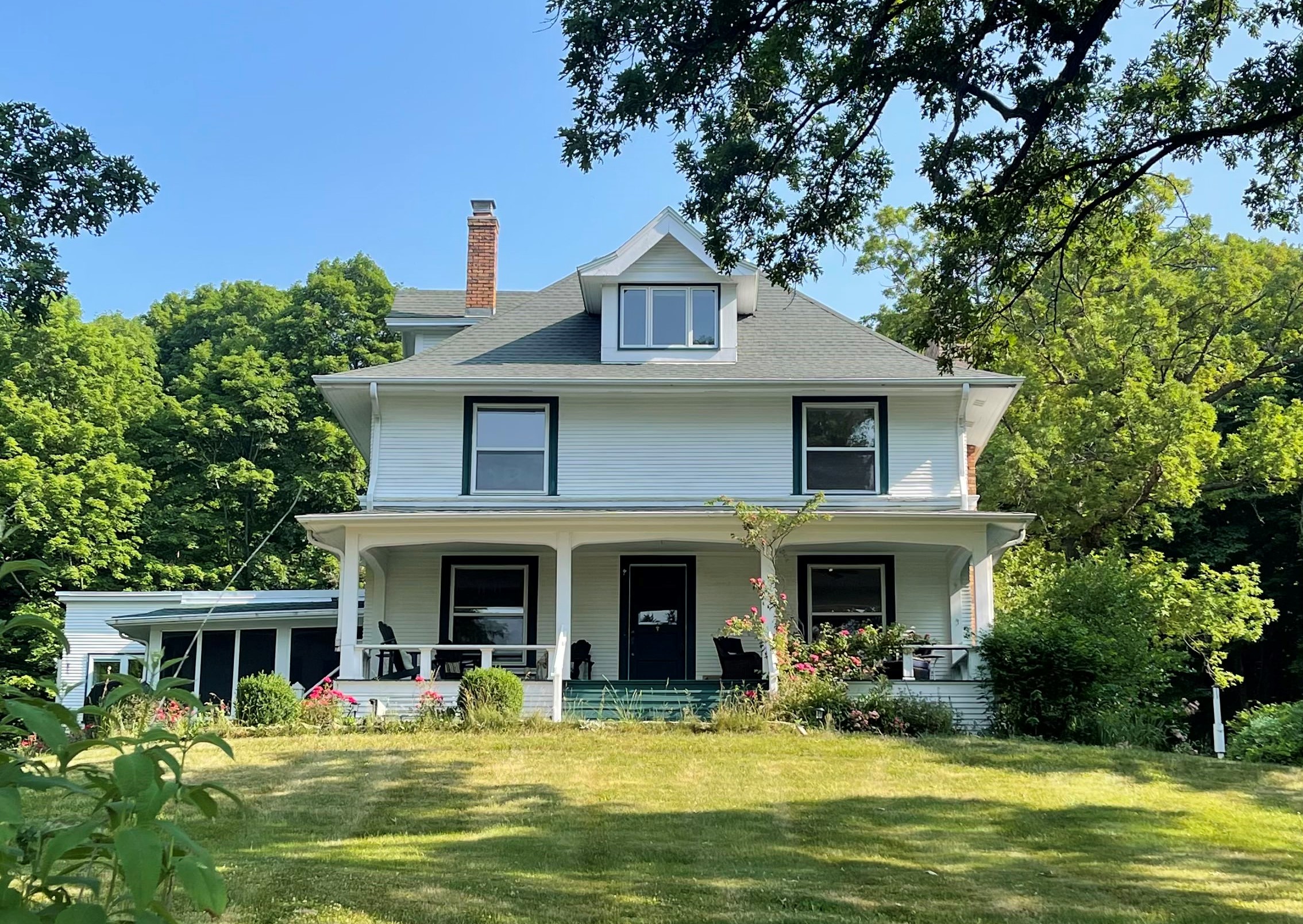 Brigham Farmhouse front of a 3 story farmhouse with porch and screened in porch