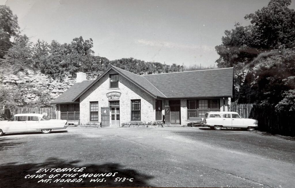 A black and white photo of a stone building with few cars parked alongside. 