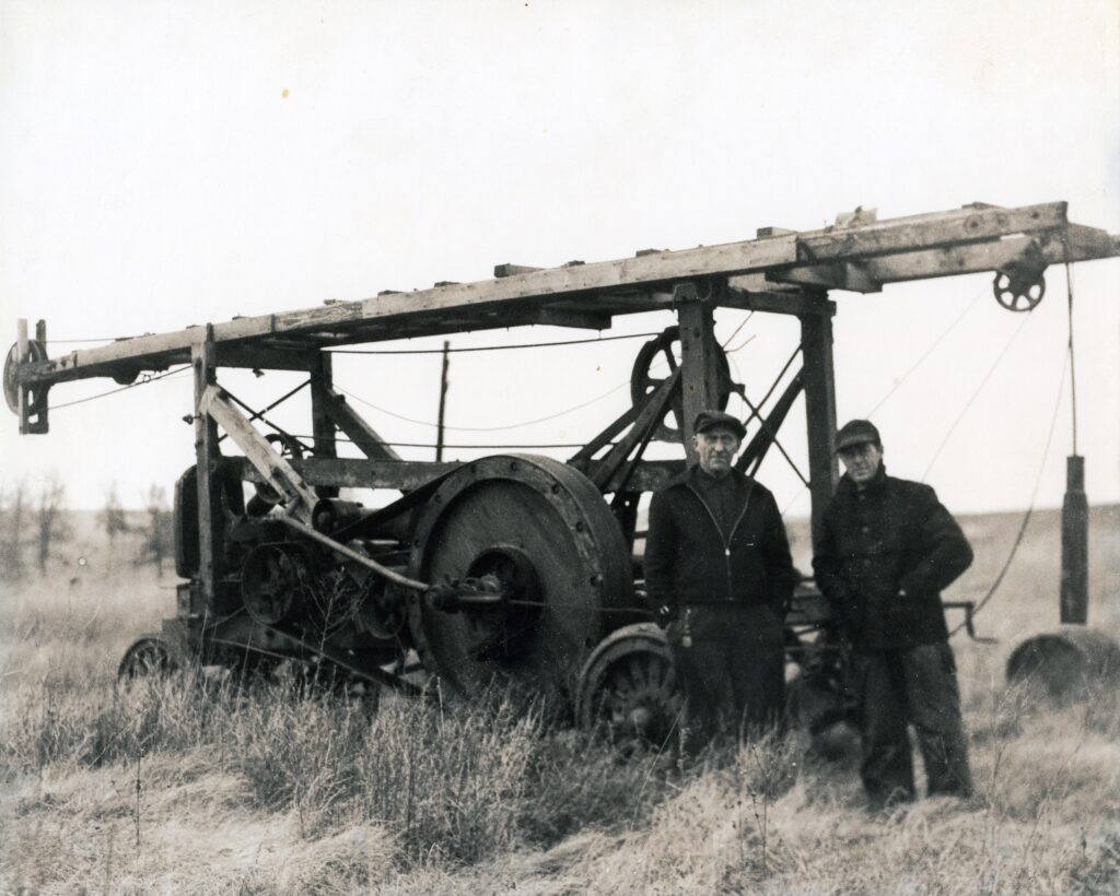 Two quarry men stand next to a large machine meant to drill holes in a quarry.