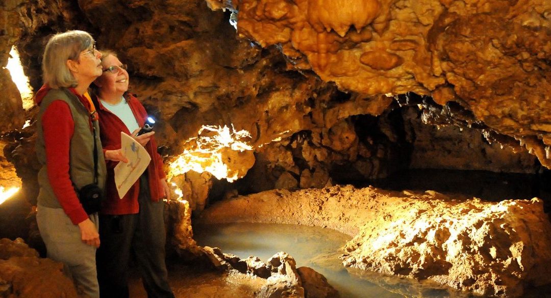 Two women exploring a cave with information brochures and a flashlight